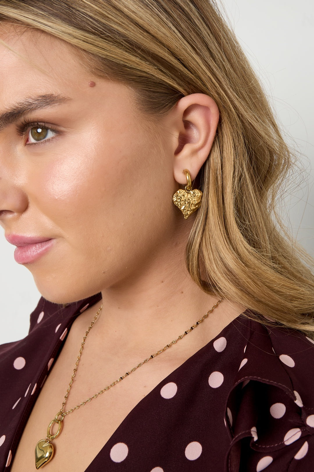 Close-up of a woman wearing gold textured heart hoop earring showing playful and youthful style