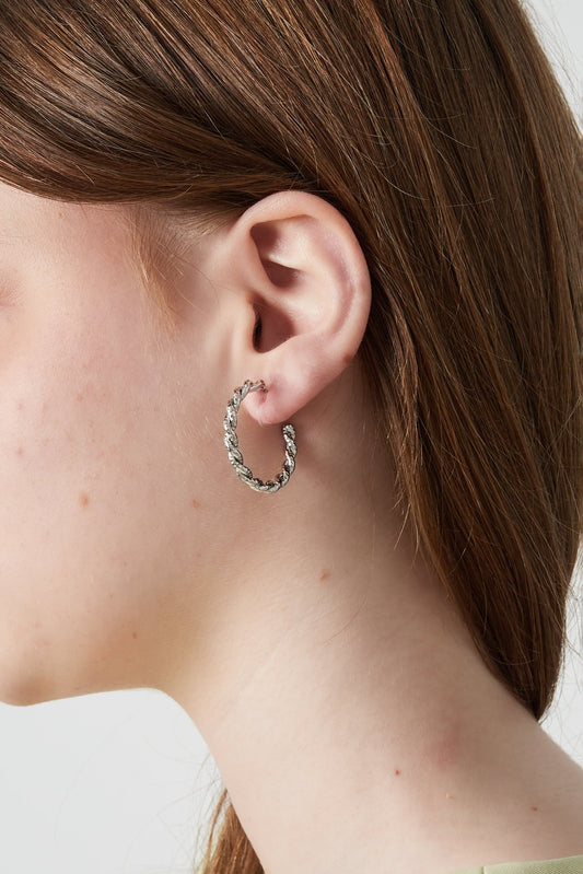Side profile of a woman wearing silver-toned twisted clip-on hoop earrings