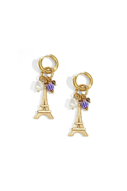 Gold-tone hoop earrings with dangling Eiffel Tower charm, white pearl-shaped bead, and purple accent bead on white background