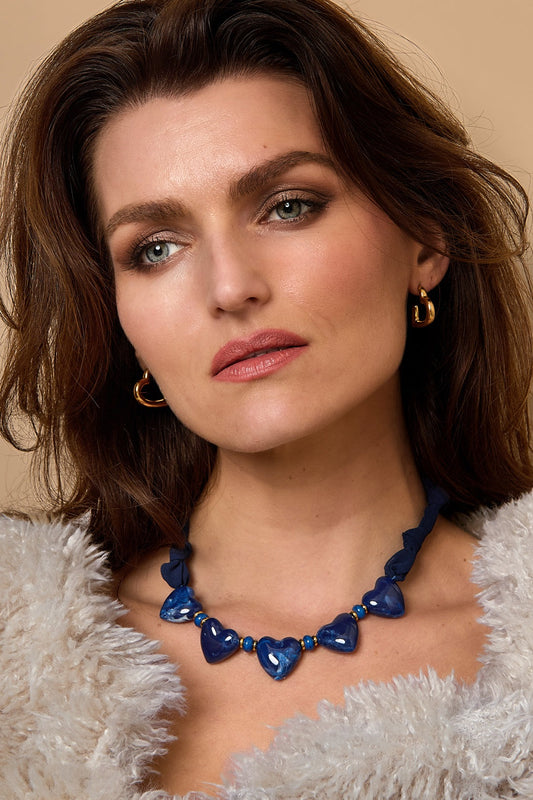 Woman wearing the navy heart bead necklace styled with a fluffy white sweater and gold hoop earrings