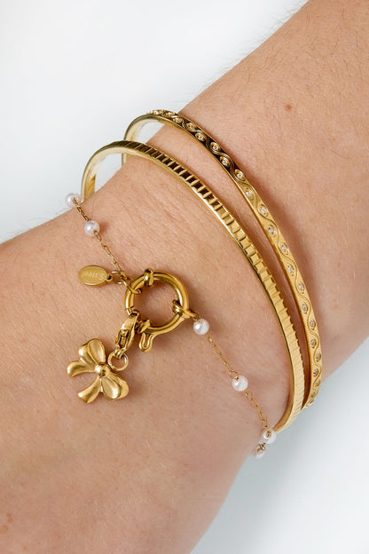 Close-up of wrist wearing three gold bracelets including delicate pearl chain bracelet with toggle clasp and bow charm