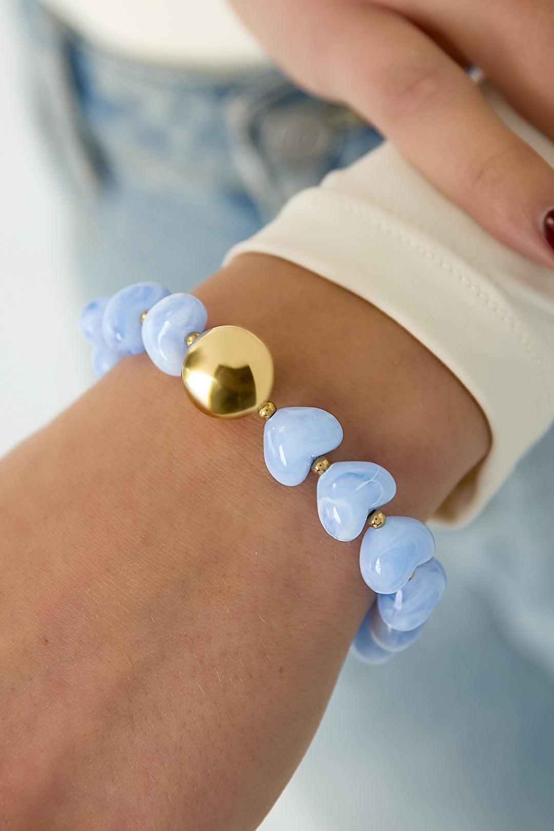 Blue heart-shaped acrylic beaded bracelet with shiny gold heart bead worn on wrist