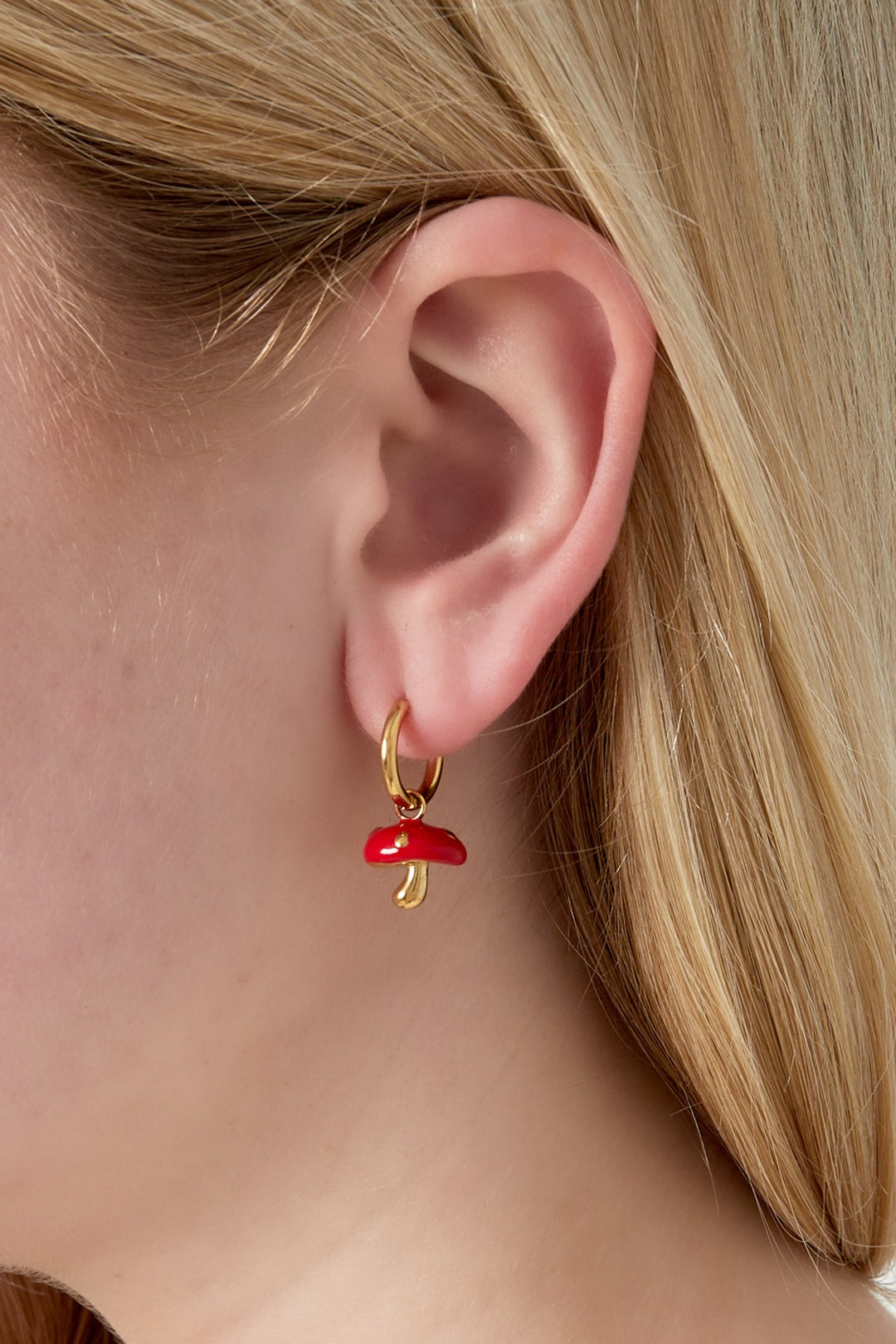 Close-up of a woman wearing a gold hoop earring with a red enamel mushroom charm