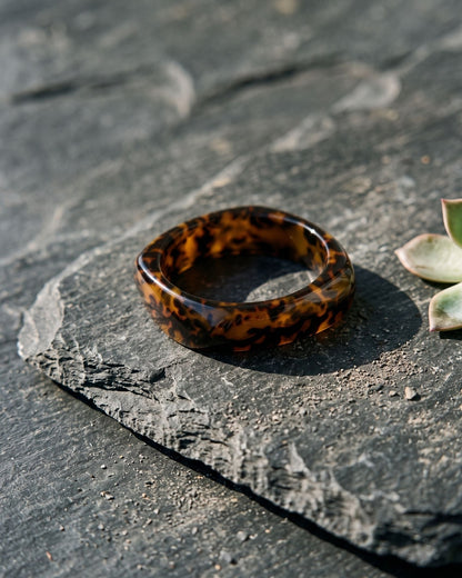Elegant brown leopard print resin bangle resting on a dark weathered slate surface.
