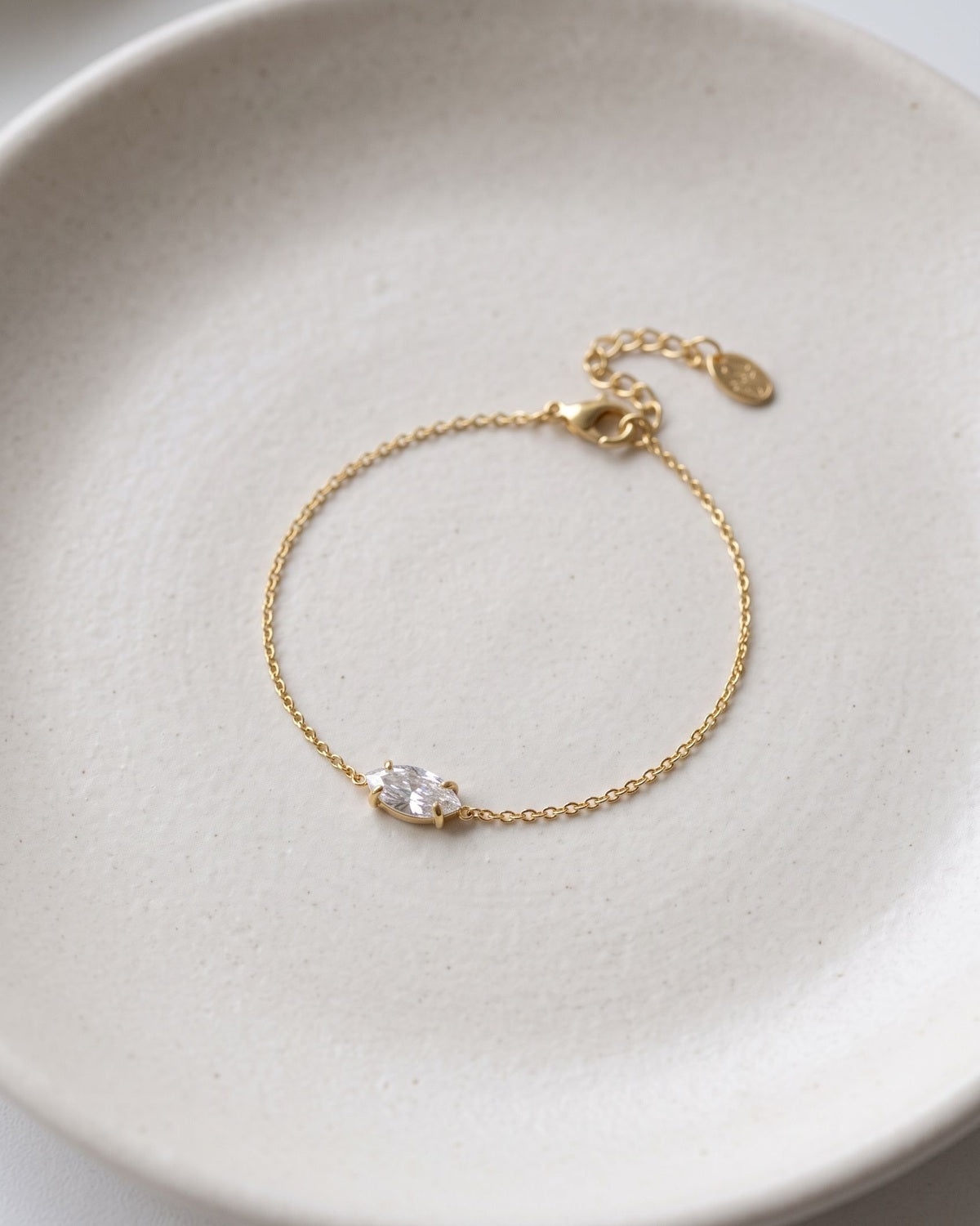 Elegant ellipse rhinestone charm bracelet displayed on a textured matte ceramic dish.
