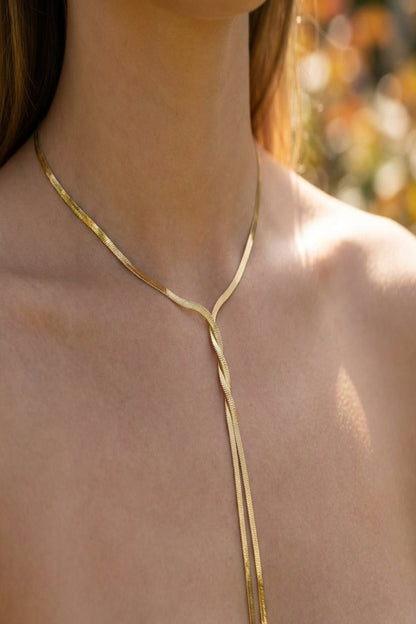 Close-up of a delicate gold twist necklace with tassel strands on a model's neck, highlighting polished finish and minimalist design in natural sunlight.