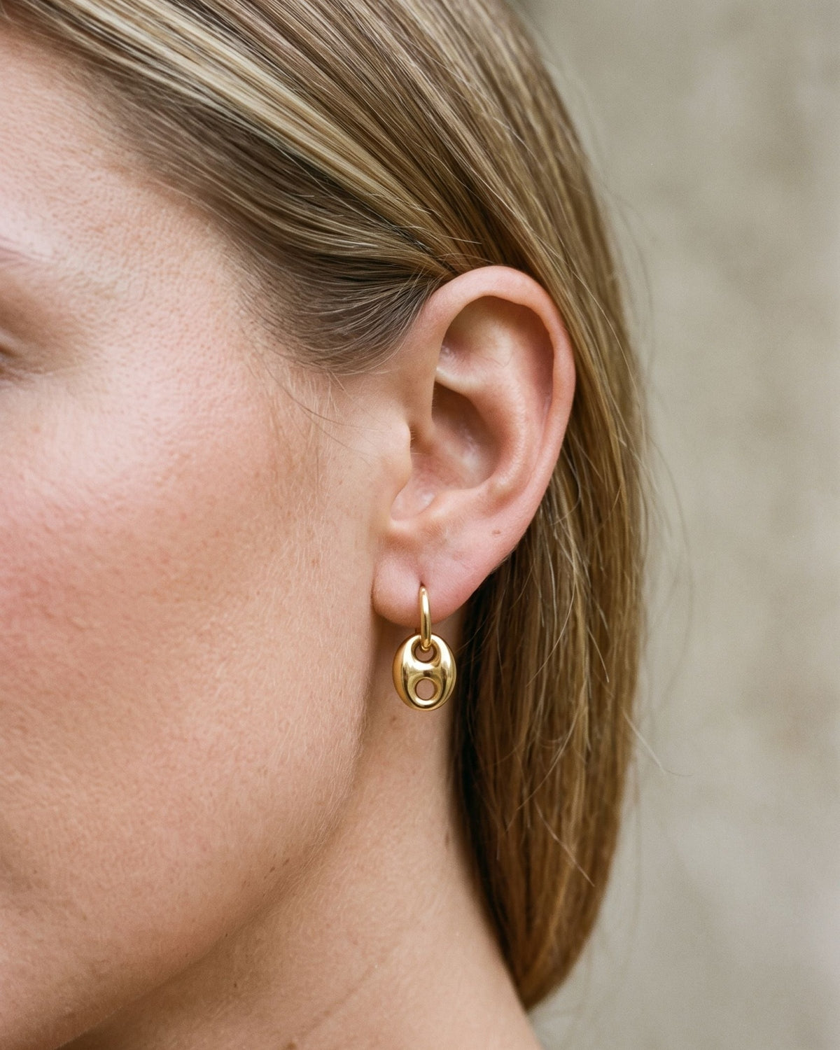 Woman wearing delicate gold irregular shaped drop earrings with a minimalist loop design for a subtle elegant look.