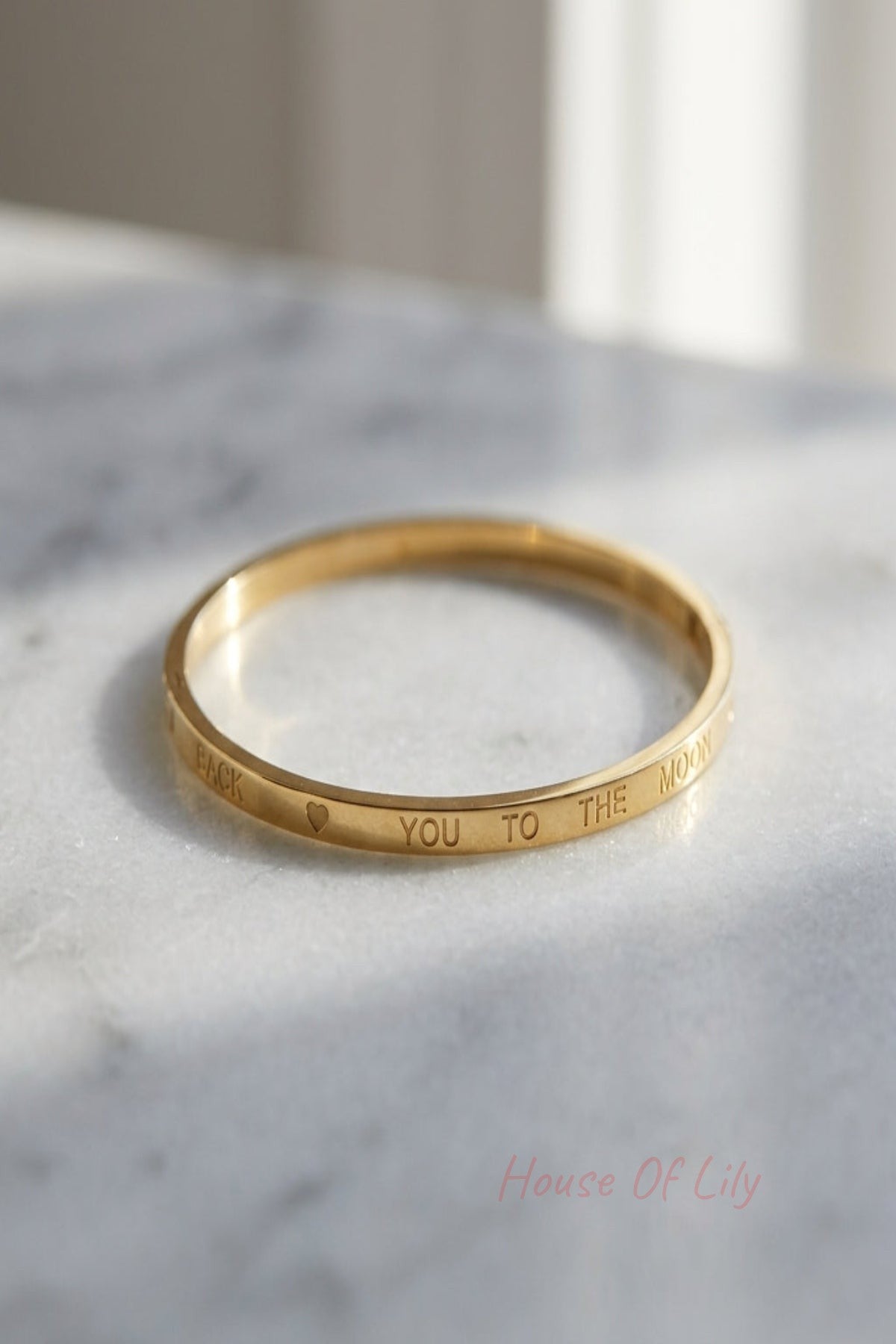 Small women's bracelet with minimalist design, displayed on a reflective surface with natural lighting and delicate lettering.