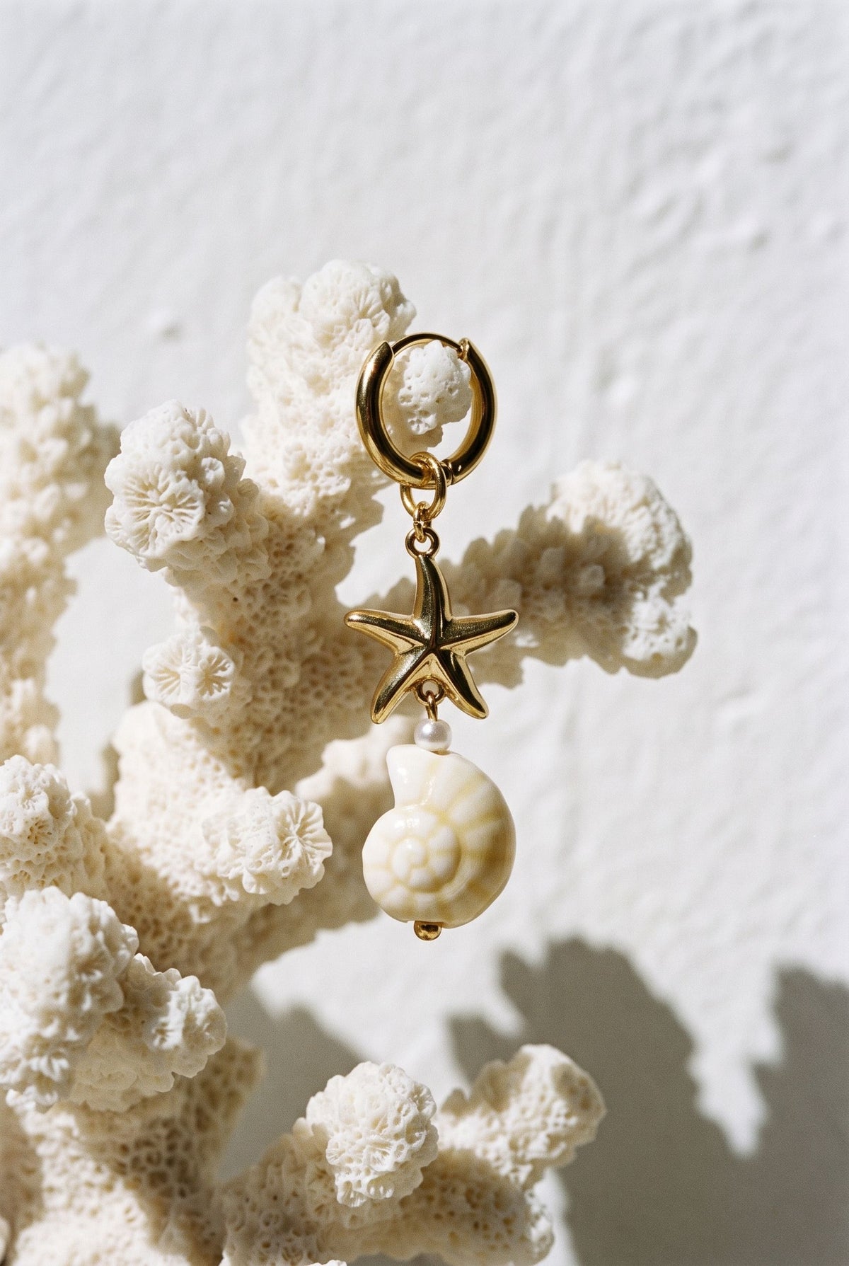 Gold-tone shell and starfish drop earring hanging from a white coral branch.