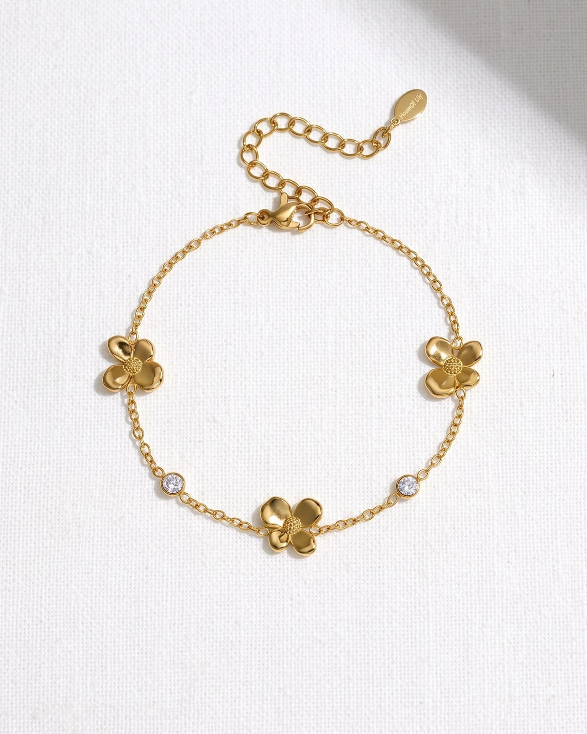 Delicate stainless steel flower charm bracelet with zircon accents resting on a textured white linen surface.