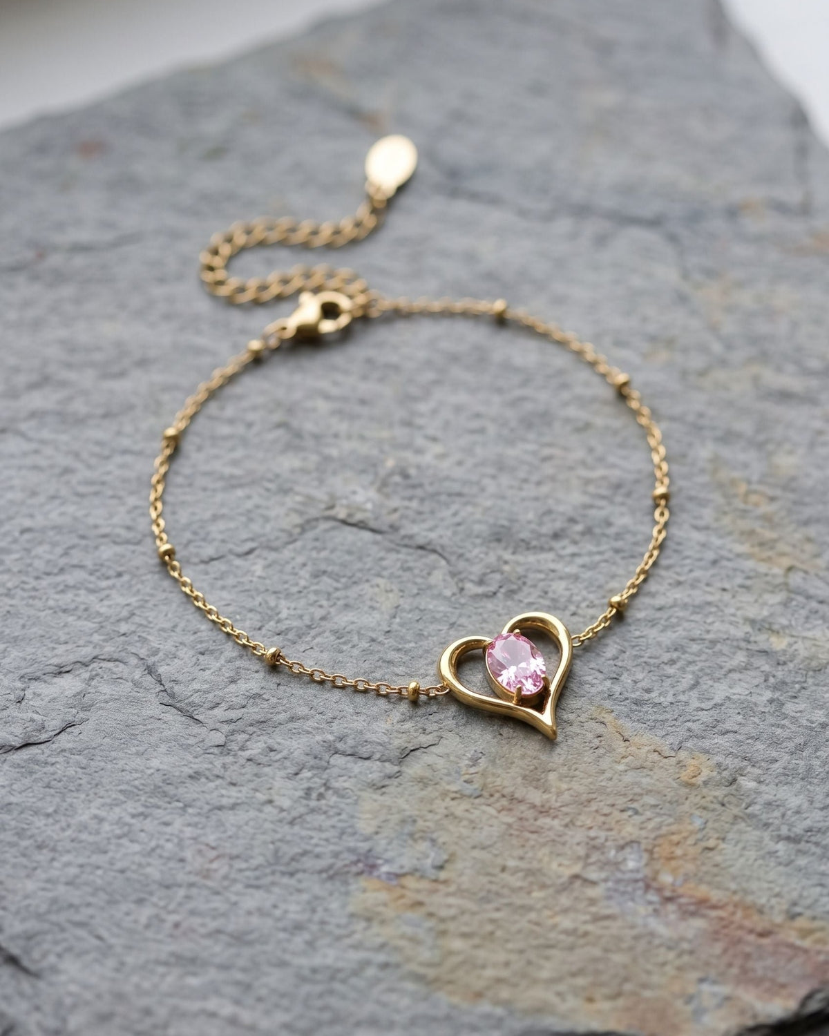 Delicate stainless steel heart charm bracelet with zircon stone resting on a grey slate surface.
