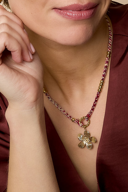 Detailed close-up of the floral charm necklace worn on neck showing woven rope and gold flower pendant