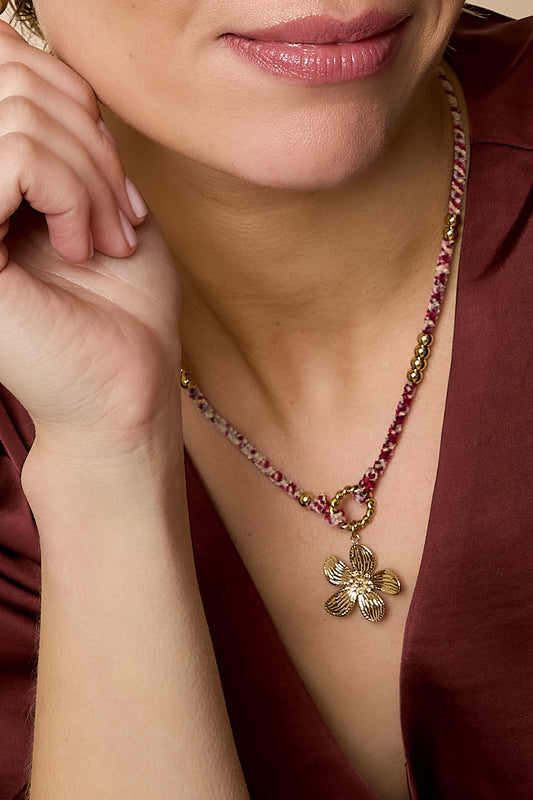 Detailed close-up of the floral charm necklace worn on neck showing woven rope and gold flower pendant