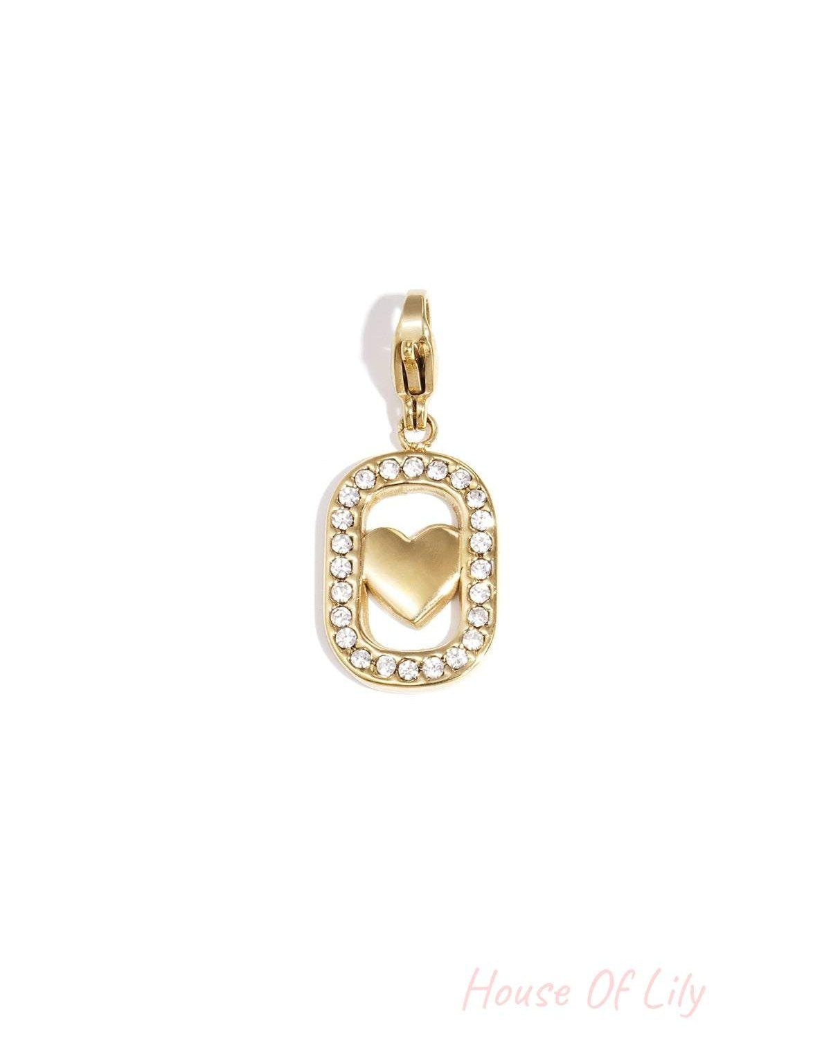 Gold-colored metal charm with a rhinestone-bordered oval frame enclosing a solid heart and a clasp at the top.