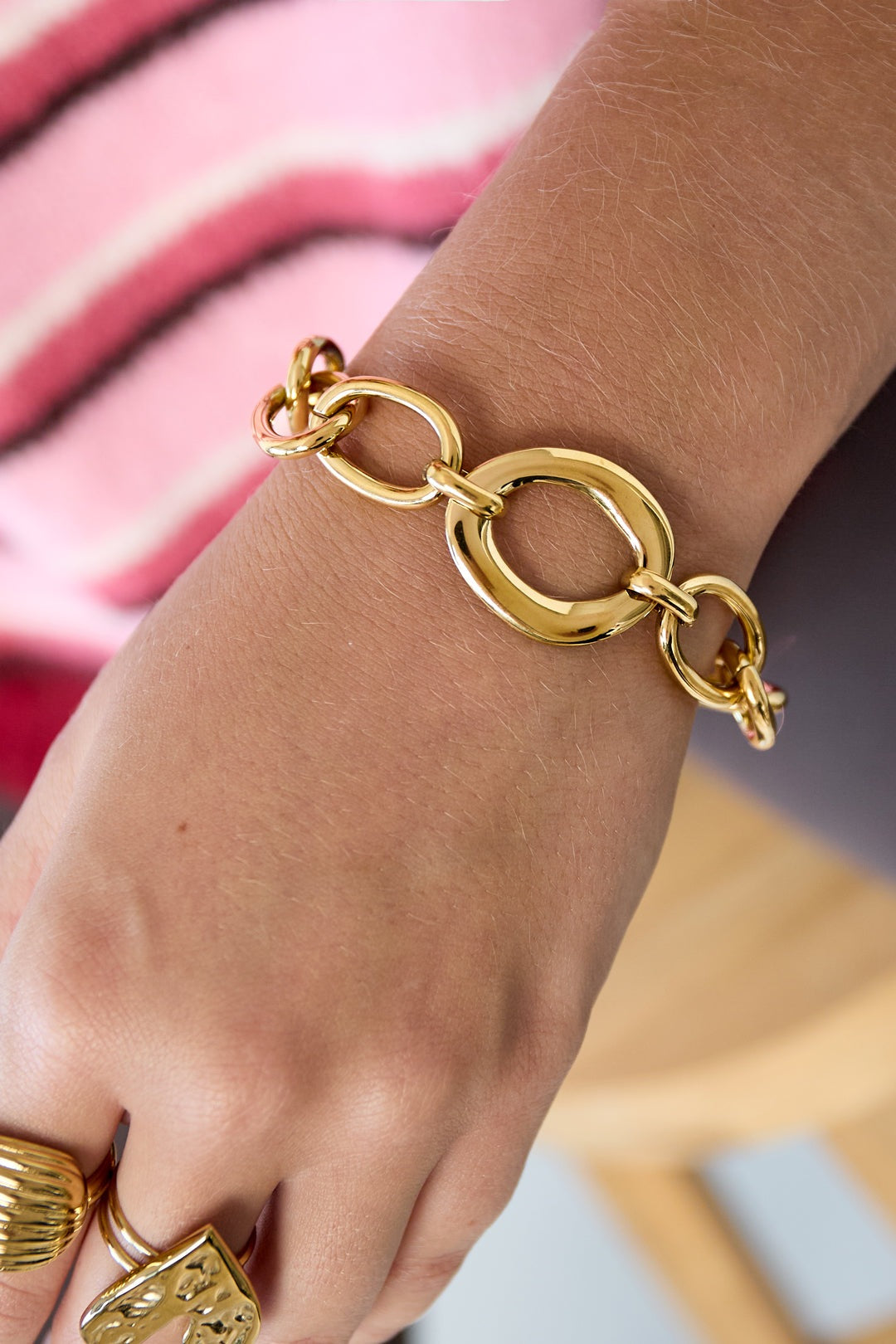 Close-up of golden chunky linked chain bracelet worn on wrist with rings