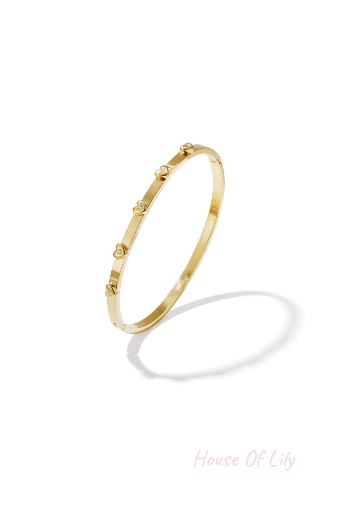 Gold-tone bangle bracelet with small heart-shaped rhinestone details displayed on white background