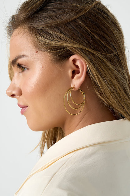 Side profile of woman wearing gold triple layered hoop earrings showcasing elegant minimalistic layered design against ivory blazer