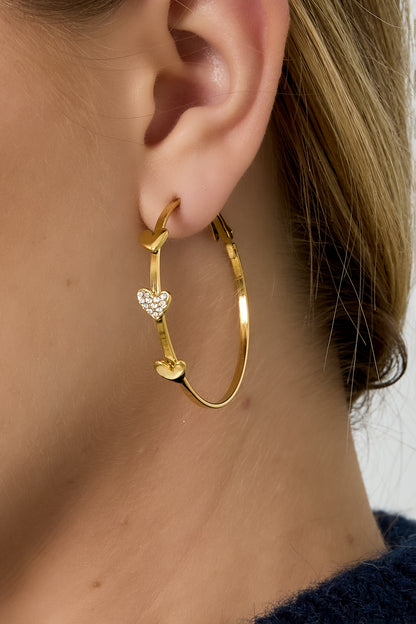 Close-up of a woman wearing the gold heart-adorned hoop earring, highlighting the sparkle and delicate design