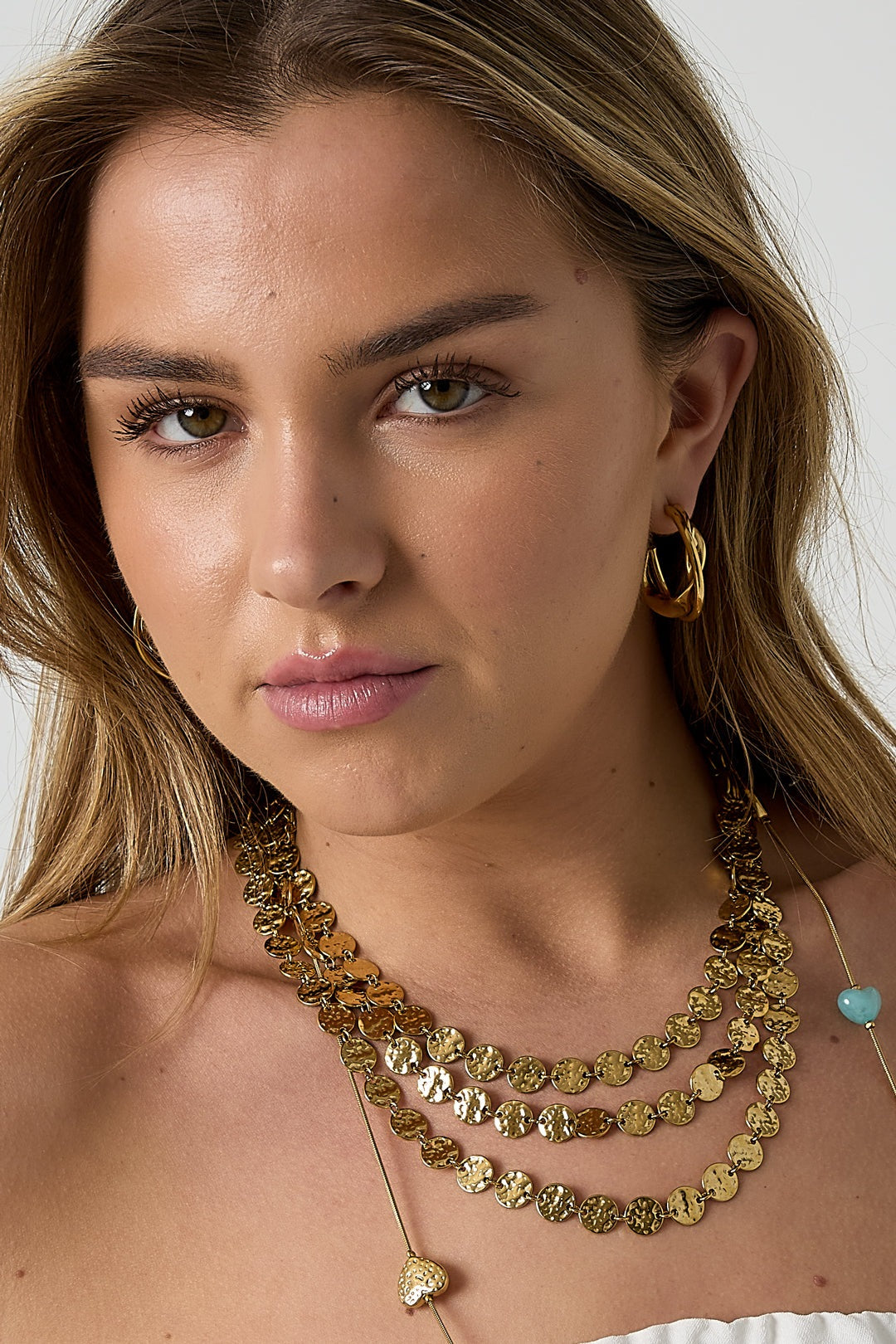 Woman wearing gold twisted double hoop earrings with layered gold necklaces