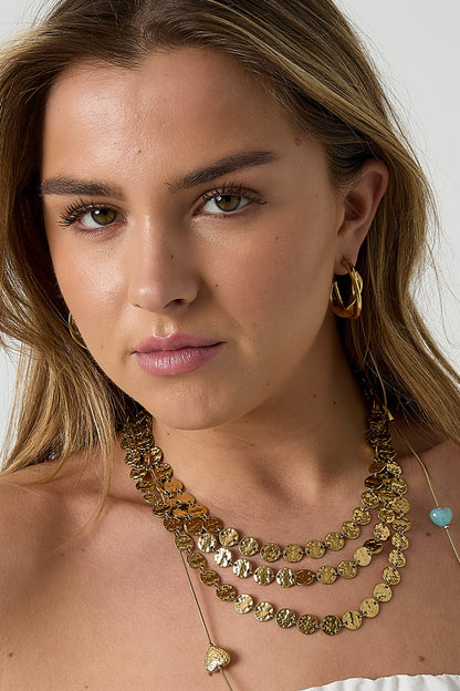 Woman wearing gold twisted double hoop earrings with layered gold necklaces