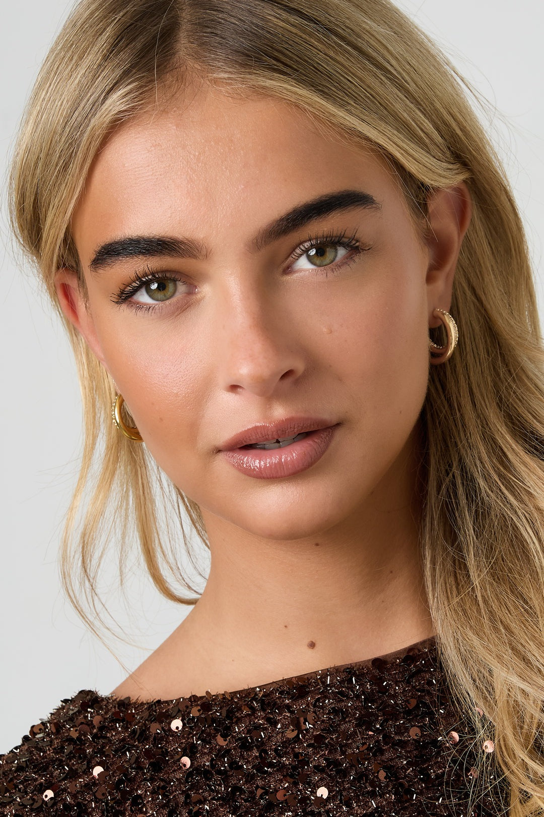 Close-up portrait of woman wearing the gold tone rhinestone hoop earrings, smiling softly