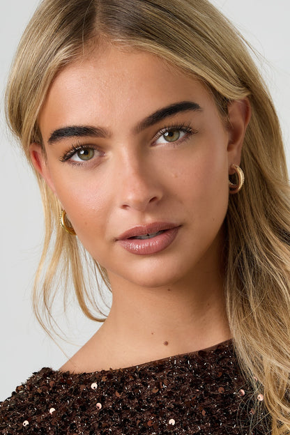 Close-up portrait of woman wearing the gold tone rhinestone hoop earrings, smiling softly