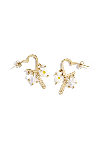 Pair of gold-tone heart-shaped drop earrings with dangling white beads, pearl-like drops, floral charms, and a LOVE tag on a white background