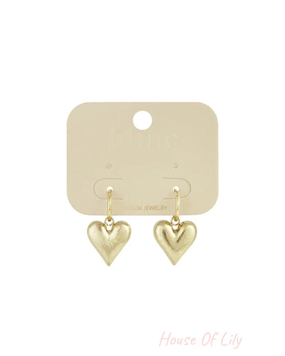 Gold-toned drop earrings with brushed-finish puffed heart pendants hanging from small hoops.