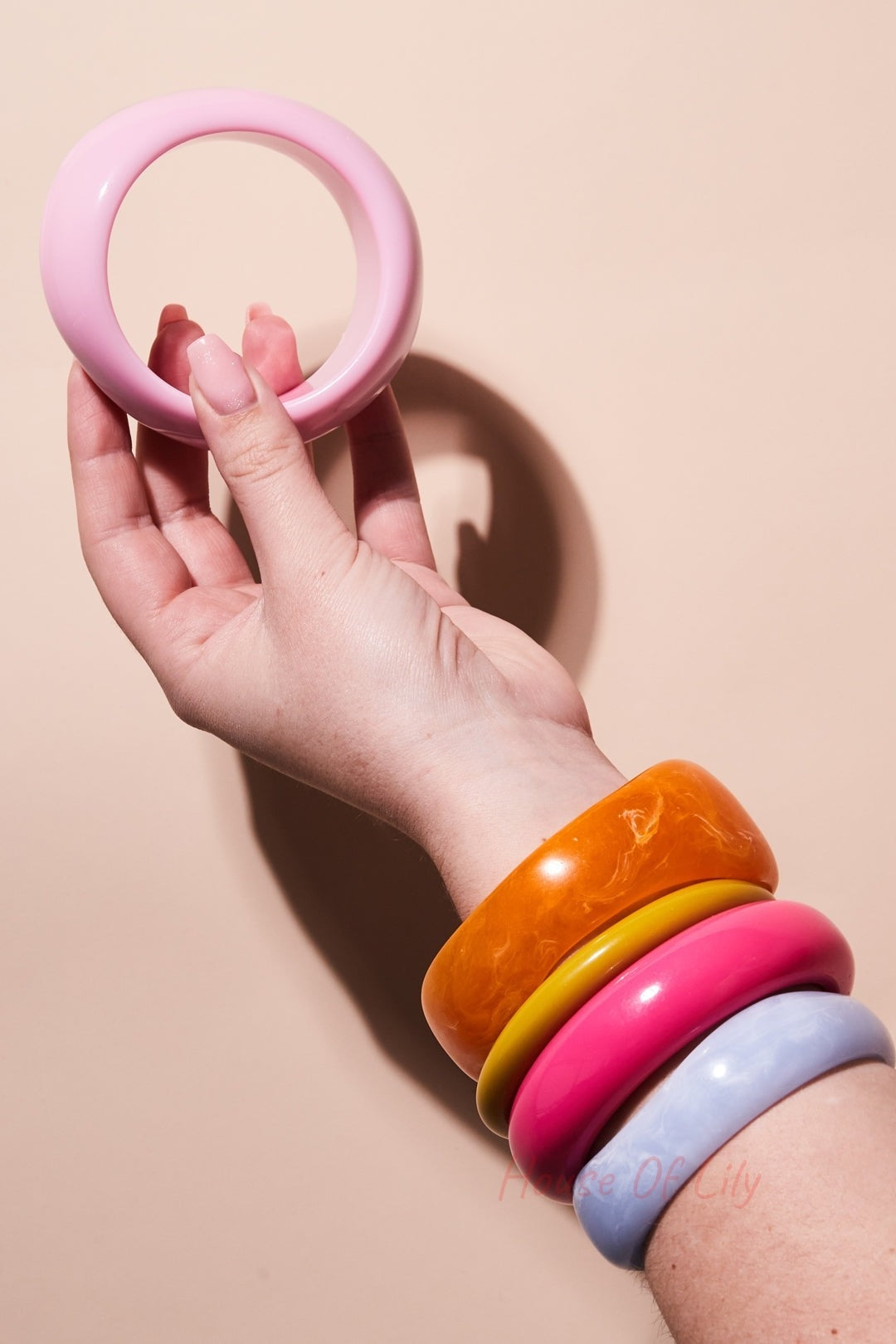 Hand holding a single pink resin bangle against neutral background with arm wearing chunky orange, yellow, pink, and light blue bangles