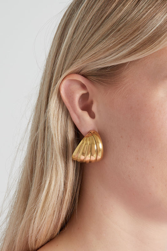 Close-up of gold sculpted hoop earring worn on a woman with blonde hair