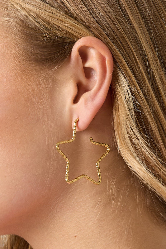Close-up of woman’s ear with gold star-shaped textured hoop earring visible