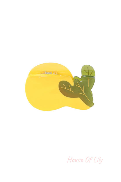 Close-up of yellow pear-shaped hair claw with green leaves detail against white background