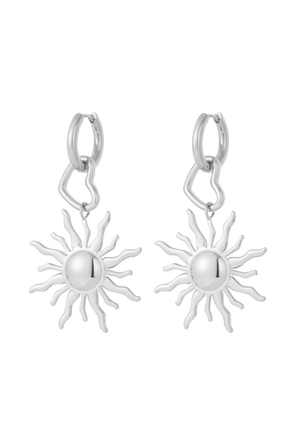 Pair of silver tone drop earrings featuring sun-shaped pendants and heart-shaped links attached to small silver hoops