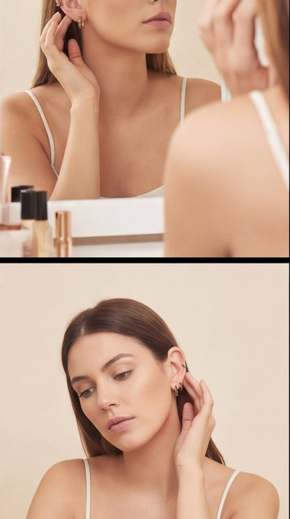 Woman adjusting earrings in front of a mirror with a neutral background