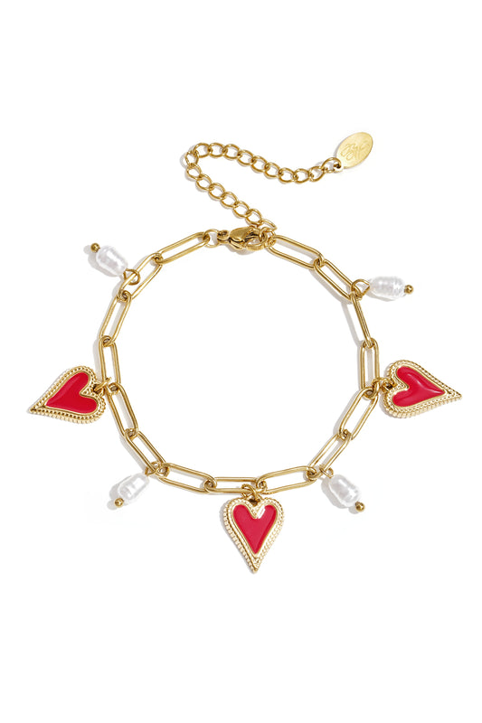 Gold chain link bracelet with red enamel heart charms and white pearl accents on a white background