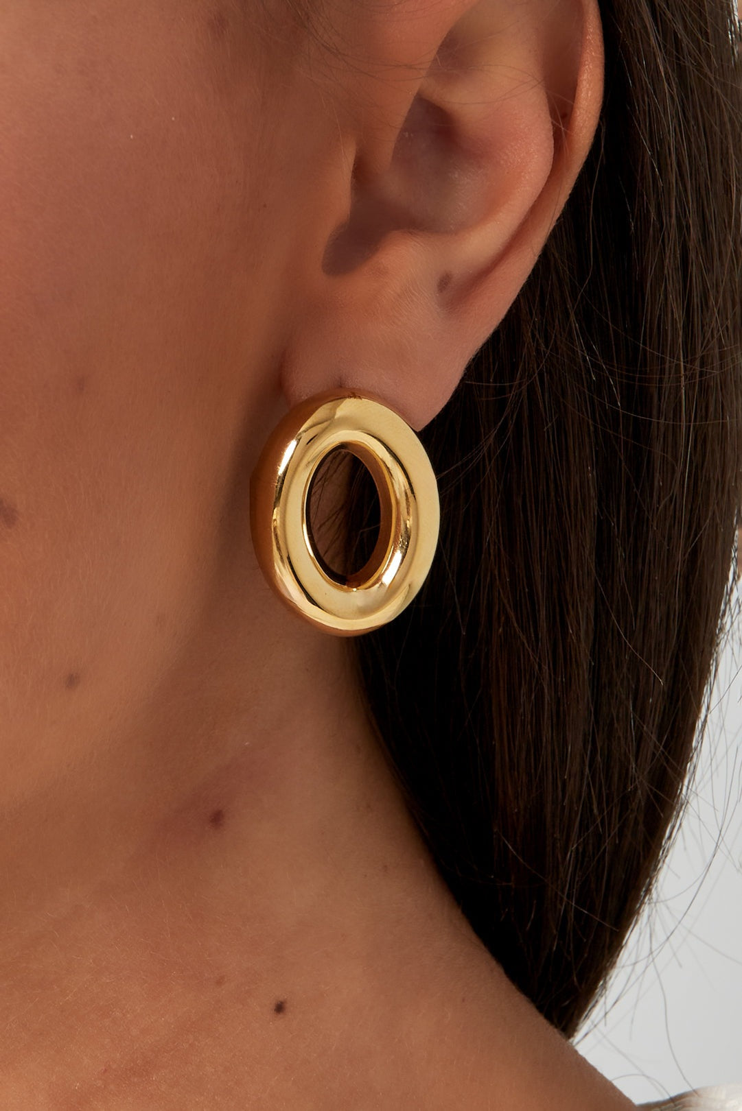 Close-up of gold open circle earrings worn on a woman's ear showcasing size and shine