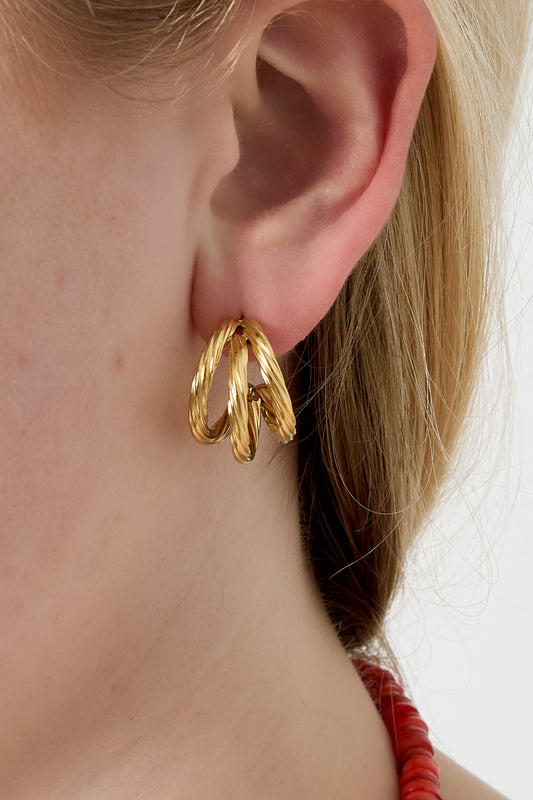Close-up of woman’s ear wearing gold twisted hoop earrings showing the unique multi-strand design