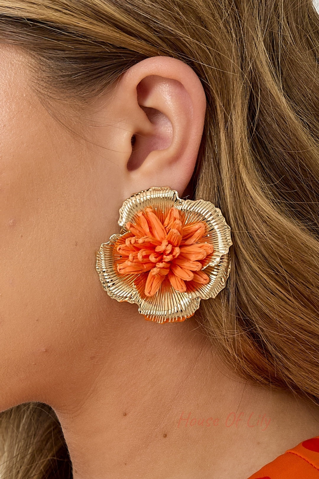Side view close-up of woman wearing orange raffia flower earrings showcasing the 3D gold-lined petal details