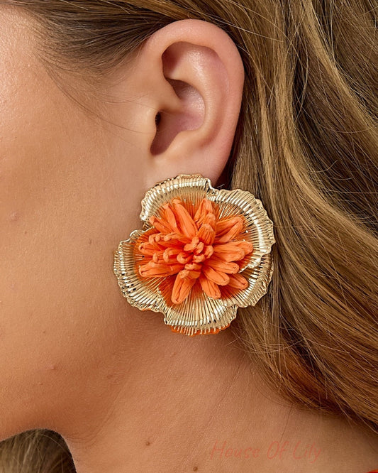 Side view close-up of woman wearing orange raffia flower earrings showcasing the 3D gold-lined petal details