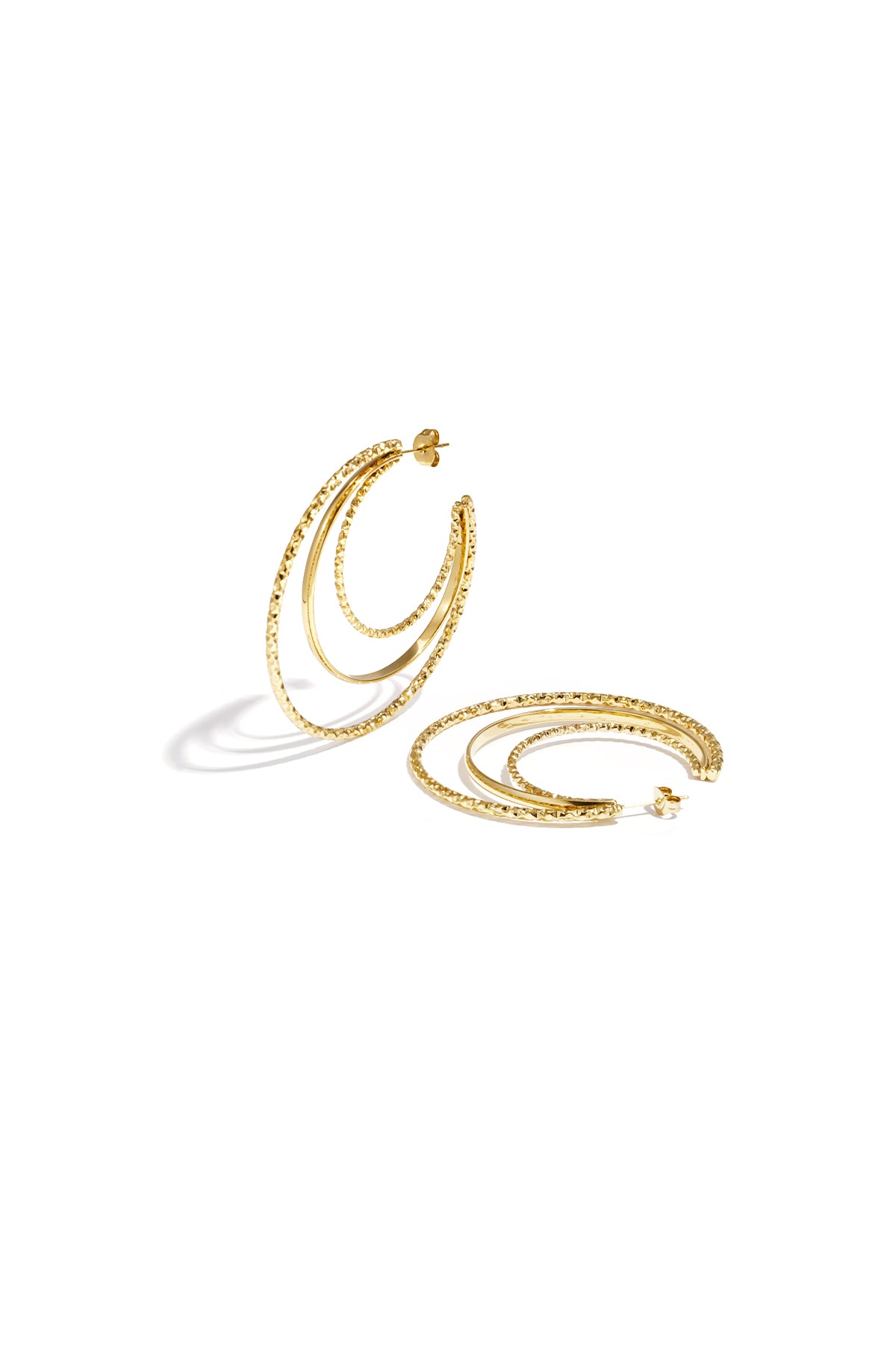Layered triple hoop earrings in gold featuring two textured hammered hoops and a smooth middle hoop arranged on a white background