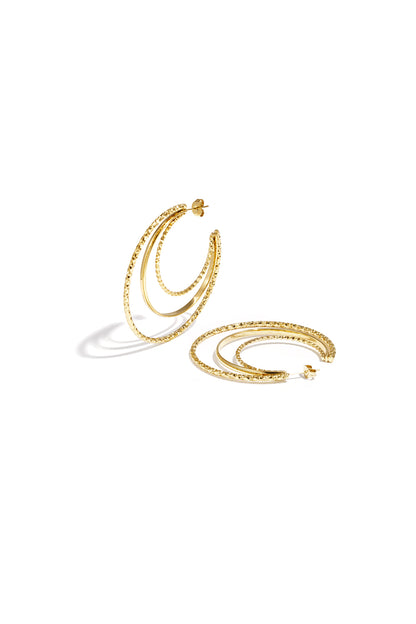 Layered triple hoop earrings in gold featuring two textured hammered hoops and a smooth middle hoop arranged on a white background