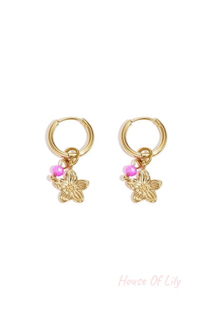 Pair of gold hoop earrings with a gold flower charm and bright pink bead on white background