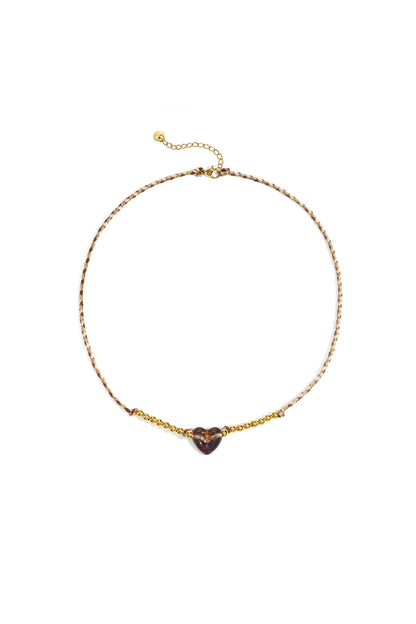 Brown and cream braided necklace with amber translucent heart bead and gold-tone beads against white background