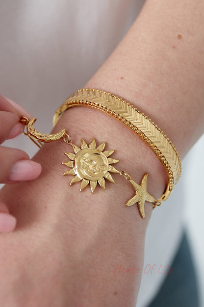 Gold chevron bangle bracelet layered with charm bracelet featuring sun and starfish charms on wrist