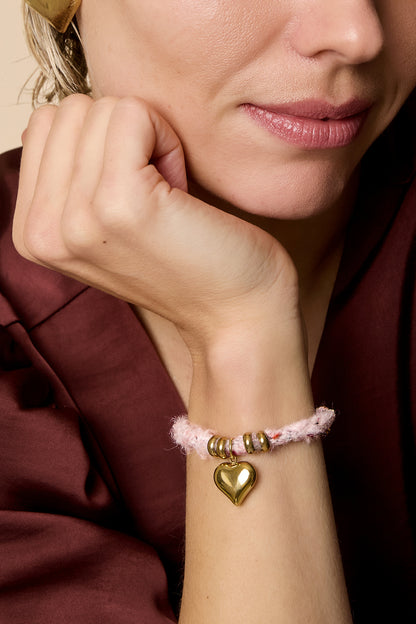 Close-up of a woman's wrist showcasing the pink knitted heart charm bracelet with gold beads