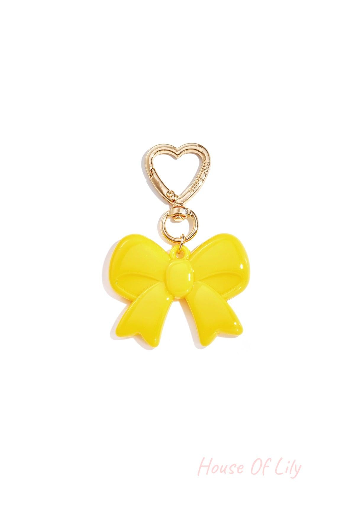 Yellow glossy acrylic bow keychain with heart-shaped gold clasp on white background