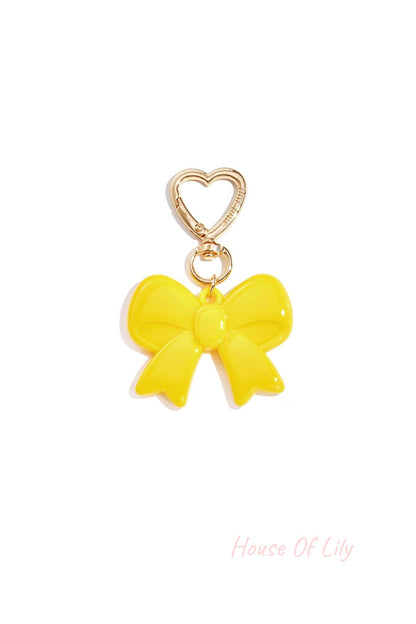 Yellow glossy acrylic bow keychain with heart-shaped gold clasp on white background