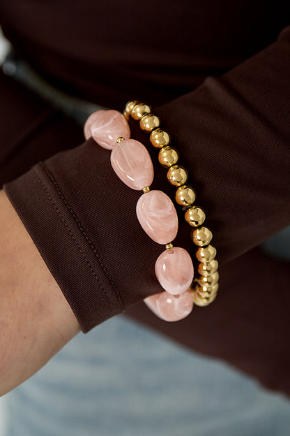 Photo of the same pink and gold-tone beaded bracelets worn on a wrist with brown sleeve and jeans