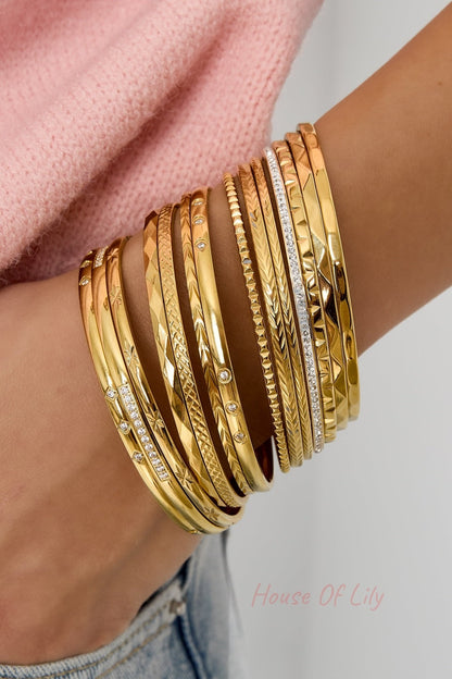 Wrist adorned with multiple gold bangles in various textured designs including one with rhinestones