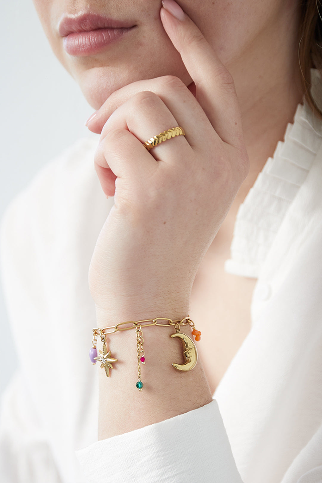 Hand model wearing the gold moonlight charm bracelet paired with a textured gold pattern ring on finger and a white blouse